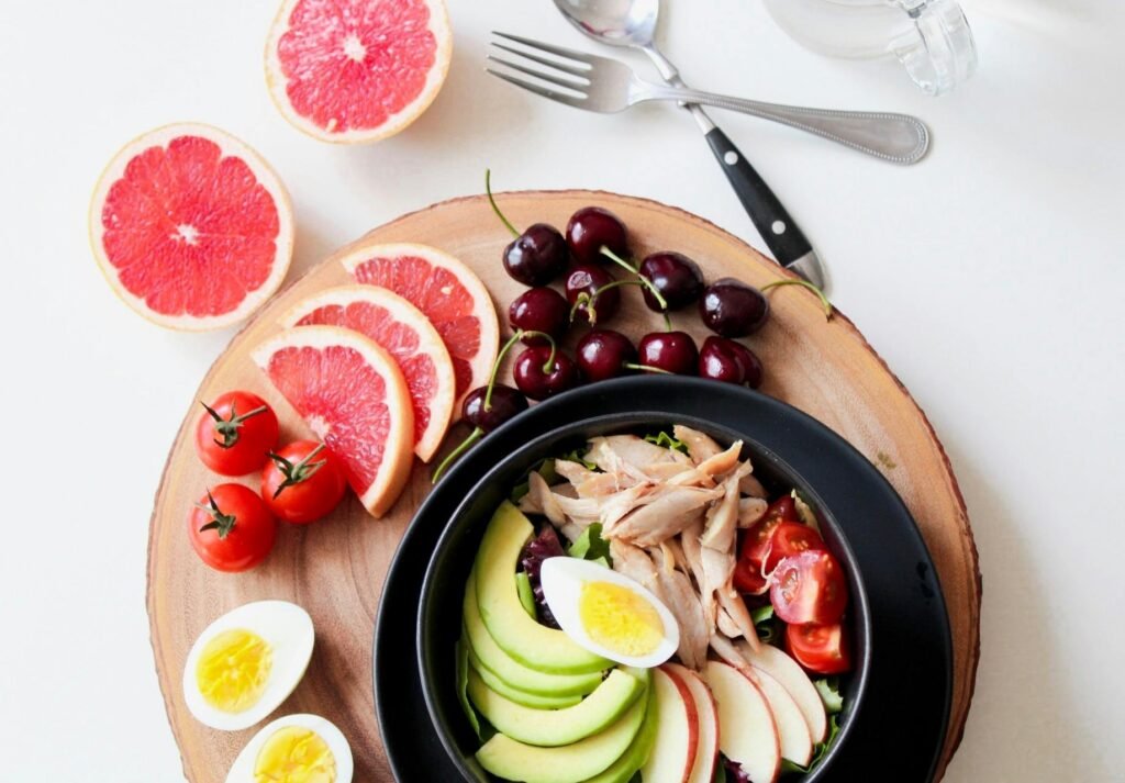 pexels-photo-936611-936611 A vibrant breakfast flat lay featuring a mix of fruits, avocado, eggs, tomatoes, and sliced meats on a wooden platter.